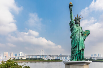 Japan, Kanto Region, Tokyo, Replica of Statue of Liberty standing against clouds with Sumida River and Rainbow Bridge in background