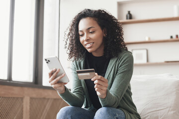 Woman holding credit card and using smartphone at home, beautiful african american girl shopping online, e-commerce, internet banking, spending money, working from home concept