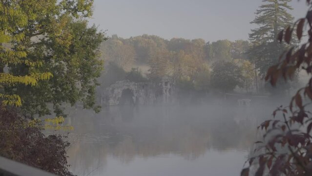 Grotto cave at Majolan Park lake in Blanquefort France with red leaf trees, Dolly right shot