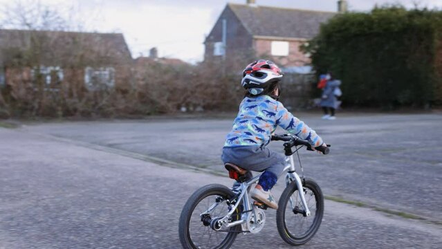 Handheld panning shot of an Asian boy riding his bike.