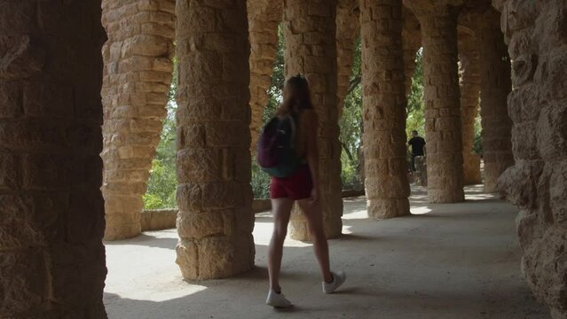 Couple Backpackers visiting the unique stone column viaduct in Parc Guell, designed by architect Antoni Gaudi in Barcelona, Catalonia, Spain - wide shot