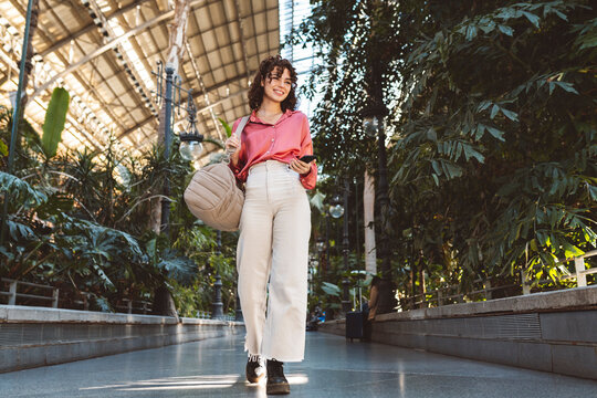 Young woman with backpack walking at station with plants