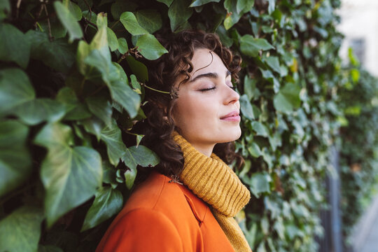 Young woman with eyes closed leaning on ivy wall