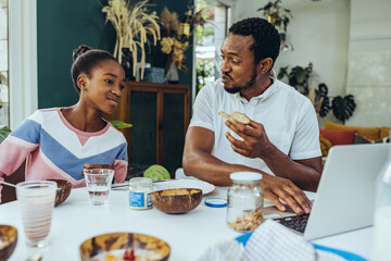Father and daughter using a laptop at breakfast table