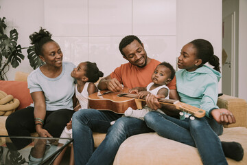 Smiling father playing guitar by family in living room