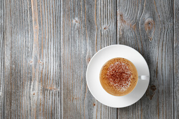 Coffee with milk sprinkled with coffee powder, copy space. Fragrant cappuccino in white cup flat lay gray wood background. Cappuccino on wooden background flat lay.