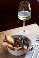 mussels with grilled bread and glass of white wine on wooden table. tasty seafood concept with dark background