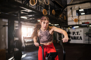 Fototapeta na wymiar Attractive masculine young woman training on the bike in the modern interior gym testing her new gym equipment wearing sportswear. Fitness girl on her leg day in the sports center. Healthy lifestyle 