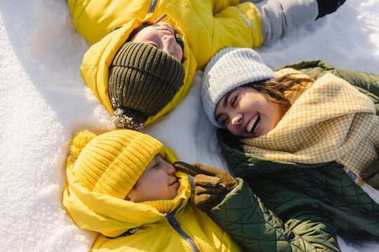Happy mother touching boy nose lying on snow in winter