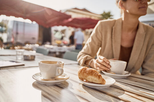 Woman holding coffee cup sitting at sidewalk cafe on sunny day