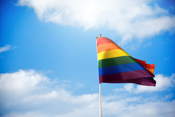 Rainbow flag, a symbol for the LGBT community, waving in the wind with a cloudy bluesky background. 