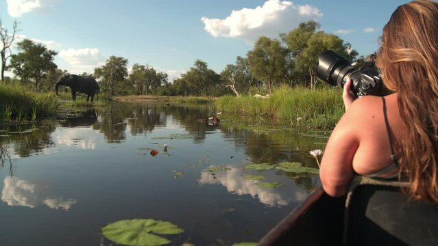 A young woman taking a picture of an elephant from a boat in a river