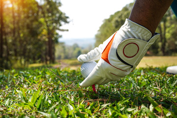 Hand ware leather glove putting golf ball on tee off, golf course background.