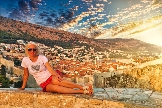 Girl sitting on top of Fort Lovrijenac fortress, over the West Harbour with Fort Bokar. Dubrovnik city walls in Croatia at sunset. Dubrovnik historic city in Dalmatia and UNESCO World Heritage Site.