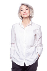 Happy trendy senior woman with a beautiful smile wearing a fashionable shirt standing with her hands in her pockets looking at the camera isolated on white background