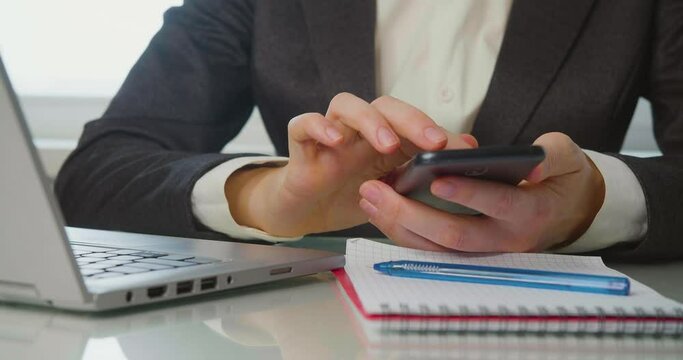Women's hands with a smartphone in the workplace. A woman scrolls, likes and looks at pictures on a smartphone during working hours.