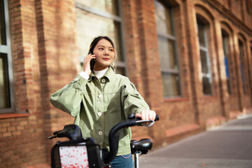 Fototapeta na wymiar Young Chinese woman talking to the phone. Beautiful happy lady with electric bicycle