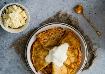 Pancakes on a plate with sour cream, golden spoon. View from above