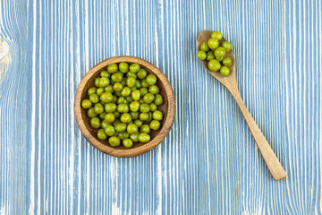 Green peas in a wooden bowl on a wooden table.