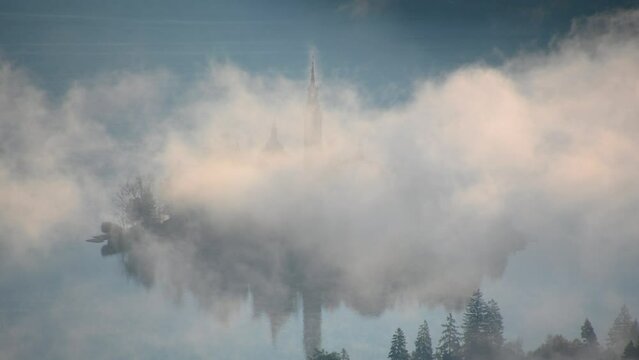 Elevated view of fog moving around small island on lake Bled, Slovenia. Aerial, telephoto perspective of famous Assumption of Maria Church tower. Fog or mist on the surface. Static shot, real time