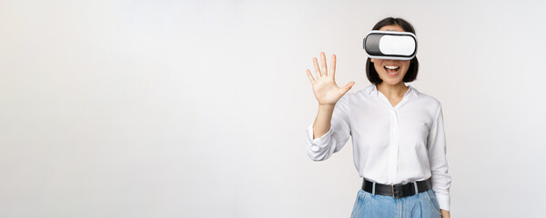 Smiling asian woman waving at you, wearing virtual reality glasses, vr headset, chatting in meta...