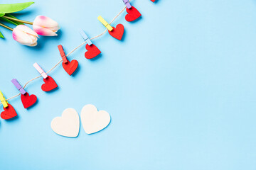 Valentine's day concept. red heart-shaped valentines decoration hanging with wood clips for happy love on the rope and white heart greeting card isolated on blue background with copy space