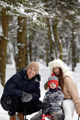 Family of mother, father and son having fun in snowy winter wood with cheerfull pet dog.