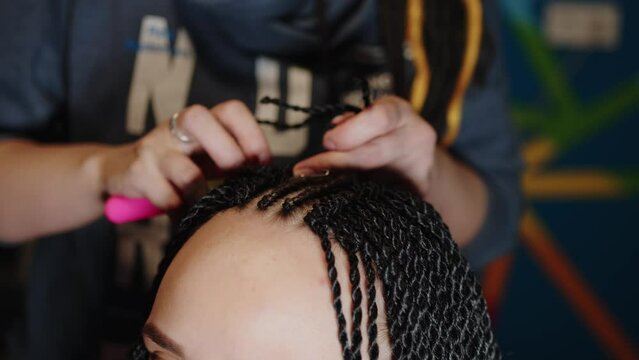 A female stylist attaches Senegalese braids to a woman in a beauty salon. Portrait of a beautiful lady with Senegalese pigtails in casual clothes. A hipster girl gets her hair done