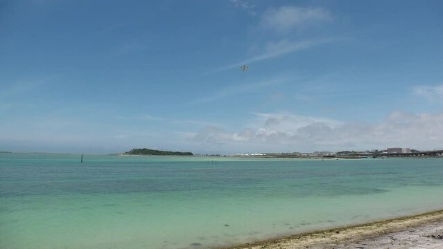 TOMIGUSUKU, OKINAWA, JAPAN - AUGUST 2021 : View of Senaga island beach (Ocean or sea) and airplane in daytime. Clear blue summer sky and clouds. Holiday, vacation and resort concept video.
