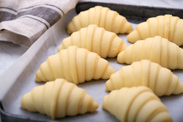 Close up of layered of a fluffy leavened uncooked traditional French croissants dough roll in a baking tray&paper sheet, preparing to cook in oven. It's a buttery,flaky, pastry
