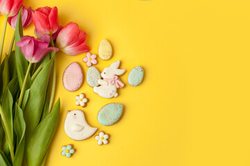 Happy Easter. Multi-colored pastel easter cookies gingerbread, seasonal flowers tulips on yellow background. Easter concept, copy space, flyer, banner, coupon, greeting card, invitation