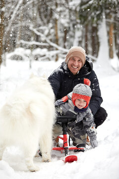 Father and son walking in snowy forest with his beagle dog in pine forest. Family walking with pets and winter outfit concept image.