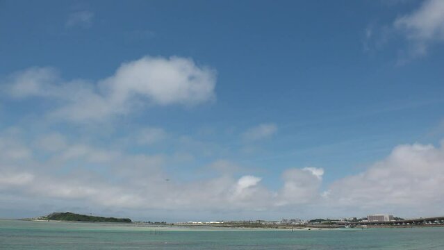 TOMIGUSUKU, OKINAWA, JAPAN - AUGUST 2021 : View of Senaga island beach (Ocean or sea) and airplane in daytime. Clear blue summer sky and clouds. Holiday, vacation and resort concept video.