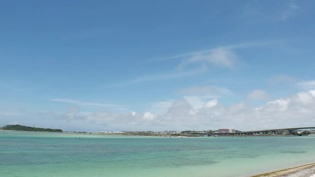 TOMIGUSUKU, OKINAWA, JAPAN - AUGUST 2021 : View of Senaga island and beach (Ocean or sea) in daytime. Clear blue summer sky and clouds. Holiday, vacation and resort concept video. Time lapse shot.