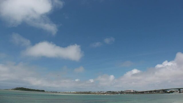 TOMIGUSUKU, OKINAWA, JAPAN - AUGUST 2021 : View of Senaga island beach (Ocean or sea) and airplane in daytime. Clear blue summer sky and clouds. Holiday, vacation and resort concept video.