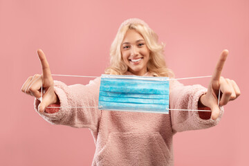 Stop covid concept. Happy woman holding medical face mask in hands and stretching it to camera over...