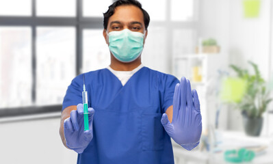 Fototapeta na wymiar healthcare, vaccination and medicine concept - doctor or male nurse in blue uniform, face protective medical mask and gloves with syringe over medical office at hospital background