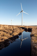 High wind power turbine in turf bog, reflection in water. Cloudy sky background. Renewable green...