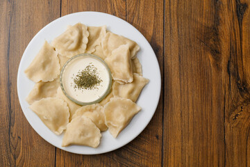 Top down view on serving of Polish dumplings and bowl with sour cream and herbs on white plate on a...
