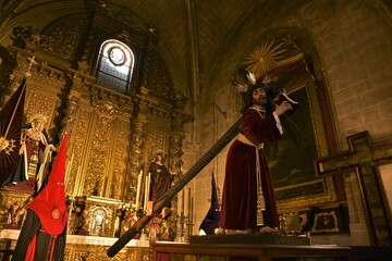 Ornately dressed sculpture of Jesús Nazareno carrying the cross, golden baroque altarpiece and red...