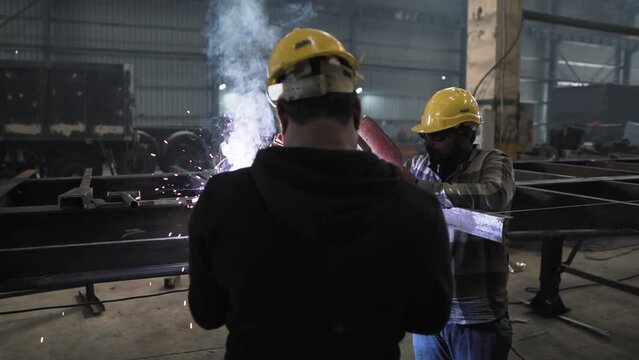 two Indian workers welding iron steel heavy metal in manufacturing production factory plant in India, technician team of working class people