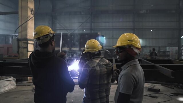 team of three Indian workers welding heavy iron steel metal in a manufacturing production line factory based in India, slow motion working class portrait