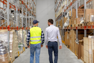 wholesale, logistic business and people concept - manual worker and businessman walking along...