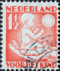 Netherlands - circa 1930: a postage stamp from the Netherlands , showing a baby with sun carried on hands. Text: For the child
