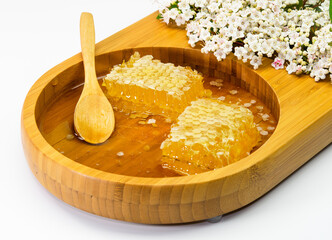 Honey with honeycomb and wooden spoon in wooden plate and white flowers on white background
