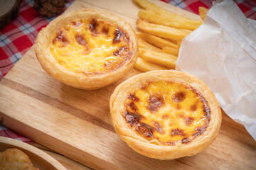 Egg tart or Portuguese egg tart in wooden plate on wooden background, Homemade egg tart and french fries dessert on wooden table.