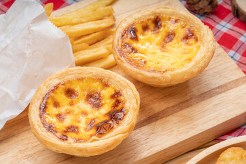 Egg tart or Portuguese egg tart in wooden plate on wooden background, Homemade egg tart and french fries dessert on wooden table.