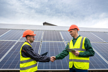 workers in  helmets two men shake hands after working on the installation of panels.