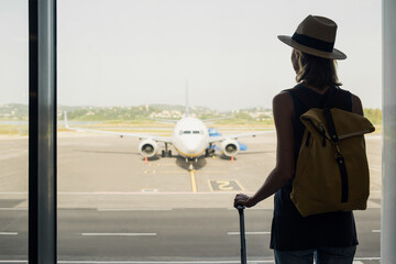 Young woman in the airport looking through the window at planes, travel, tourism, transportation,...