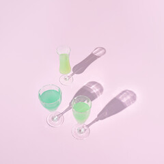 Creative arrangement with green cocktails on pastel pink background. Sunny day shadow. Minimal party or refreshment concept.
